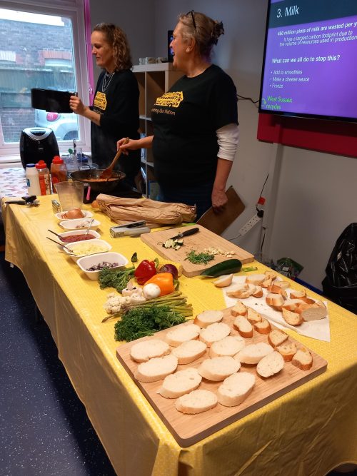 Two staff members from UK harvest demonstrating how to make food tasty and cheaply to residents