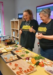 UK Harvest two members of staff smiling with their thumbs up with food prepared on the table in front of them