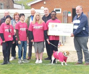 A group including resident Mapalo, wearing pink YMCA DownsLink Group tshirts holding an extra large check
