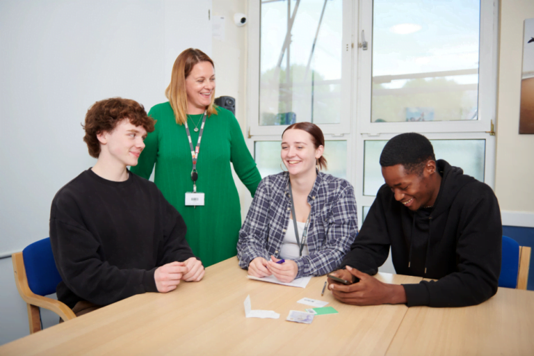 mental health awareness week: 3 young people sat at a table laughing and talking with one member of staff stood behind smiling