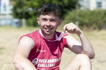 Josh smiling and holding up his medal after completing the DownsLink Challenge