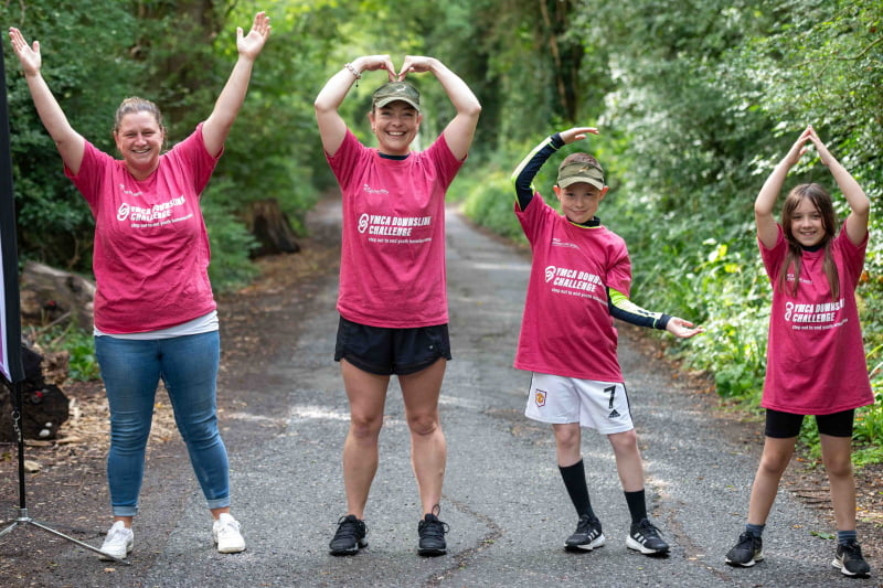 A group of four people taking part in the DownsLink Challenge. They have their arms in the air making the shape of 'YMCA'
