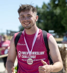 One of our nominees for the Youth Matters Awards, Josh, standing smiling with his thumbs up wearing a medal after completing the DownsLink Challenge