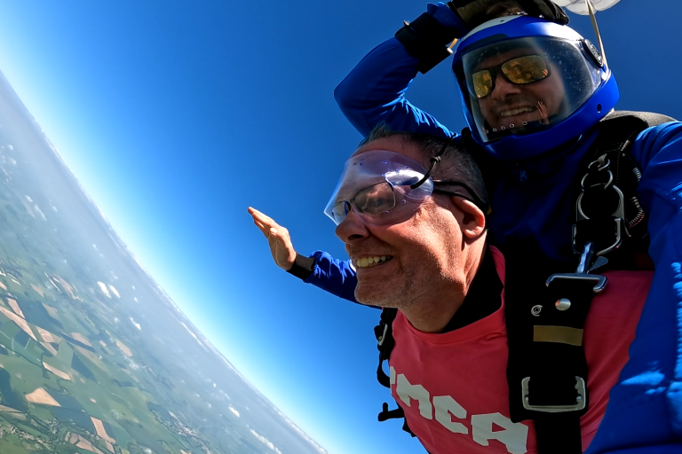 Two men doing a tandem skydive, both are falling through the sky with their arms stretched out to the side.