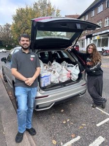 two people stood in front of an open car boot filled with donated groceries