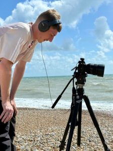 young man bent over a camera on a beach