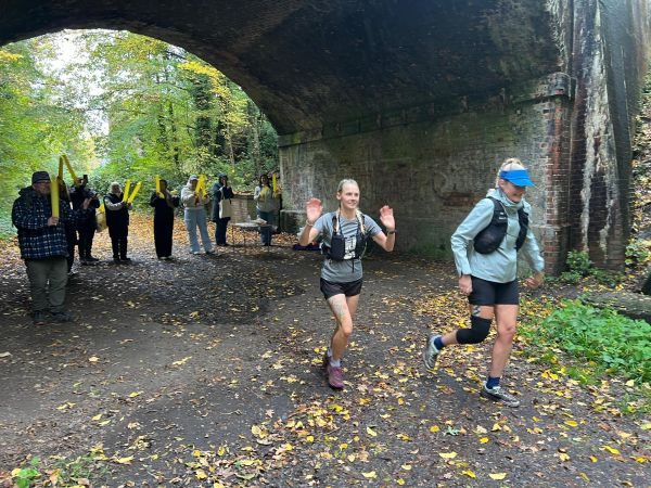 two female runners under an archway with supporters in the background