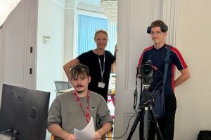 two youn gmen and one adult woman smiling with video equipment