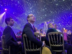 three people sat at a table looking up at a screen to the right