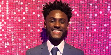 Adi smiling at the Youth Matters Awards with a pink glitter background
