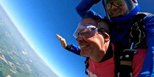 Two men doing a tandem skydive, both are falling through the sky with their arms stretched out to the side.