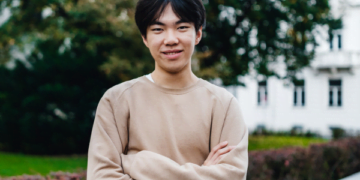 Image of Leo smiling with his arms crossed, wearing a beige jumper