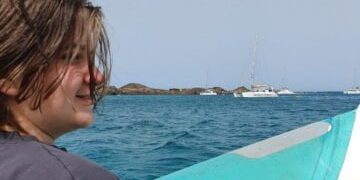 Sam sat on a boat with the sea behind him and a white boat in the distance