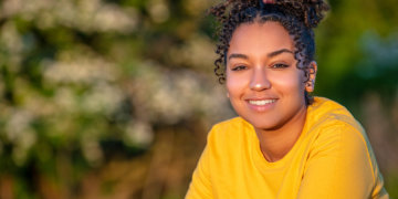 Image of young woman smiling with brown hair, wearing a yellow tshirt.