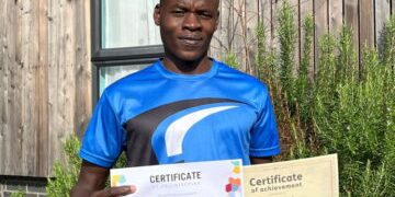 Nader stood in the garden in a blue sports tshirt holding up two certificates of achievement