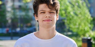 A young man Liam, stood outside wearing a white t-shirt